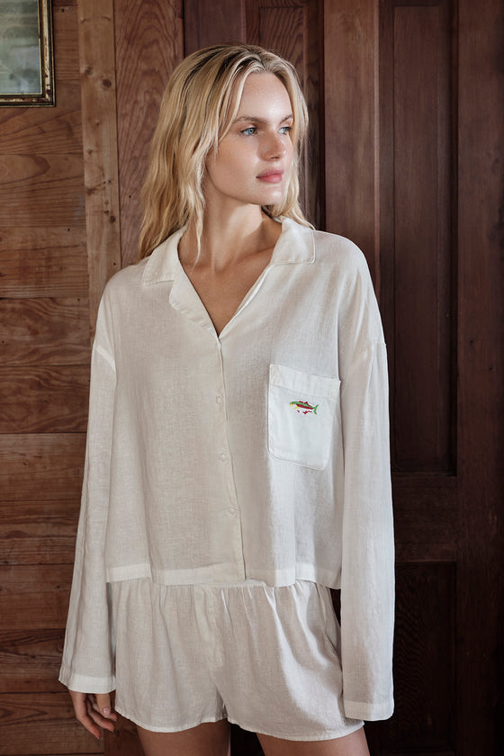 Woman wearing a white linen pajama shirt and shorts against a wooden background
|M1