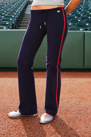 A person wearing navy athletic pants with a red side stripe and a small yellow logo, standing on an outdoor court with stadium seating in the background.
|M1