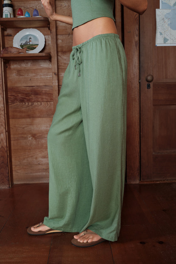 Person wearing green pants standing in a room with wooden furniture.
|M1