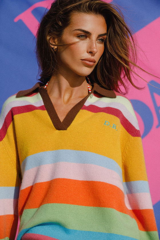 Woman wearing a colorful striped sweater with a brand logo against a vibrant background
|M2