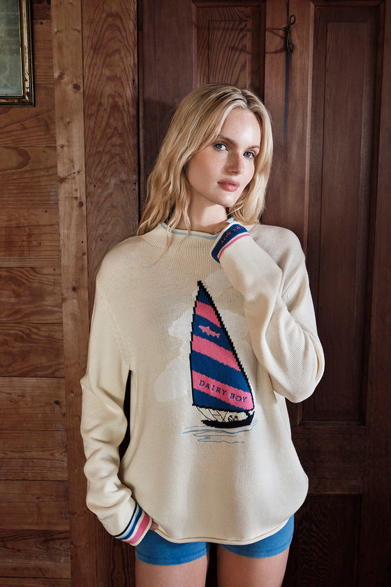 Woman wearing a cream sweater with a sailboat design against a wooden background
|M1
