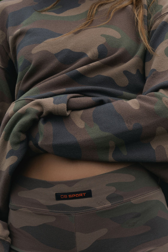 Close-up of a person wearing a camouflage sweatshirt and matching leggings, with a visible waistband label reading DB SPORT.
|M1