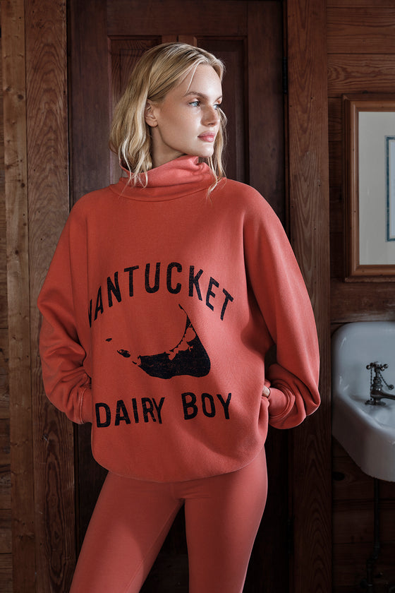 Person wearing a red 'Nantucket Dairy Boy' sweatshirt in a rustic setting.
|M1