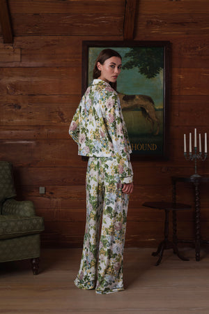 Back view on a model of a floral pajama set: long-sleeve collared top and wide-leg pants in green, pink, yellow and blue flowers with dark piping. |M2