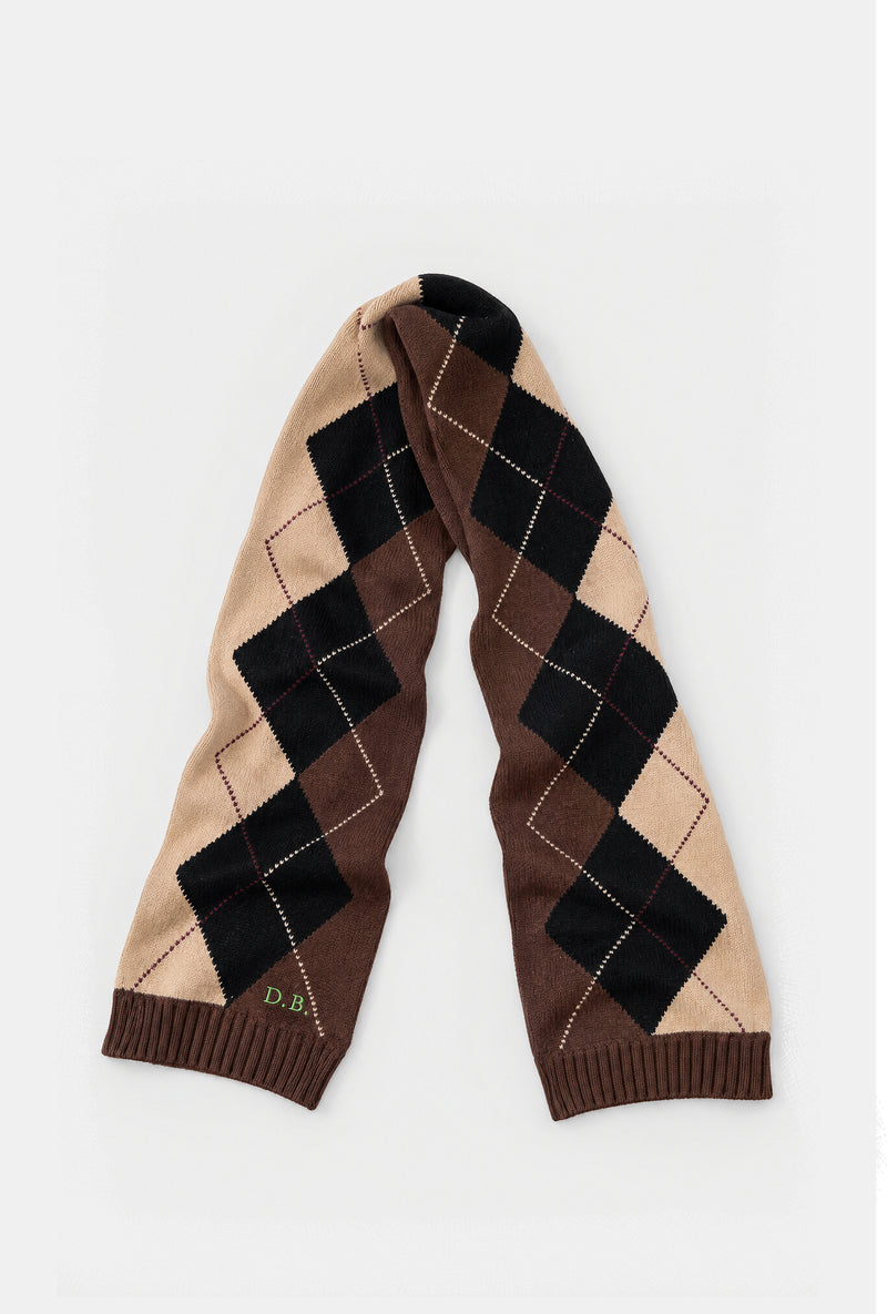 A knit scarf with an argyle pattern in beige, brown, and black, featuring ribbed cuffs and a small embroidered 'D.B' logo on the cuff.