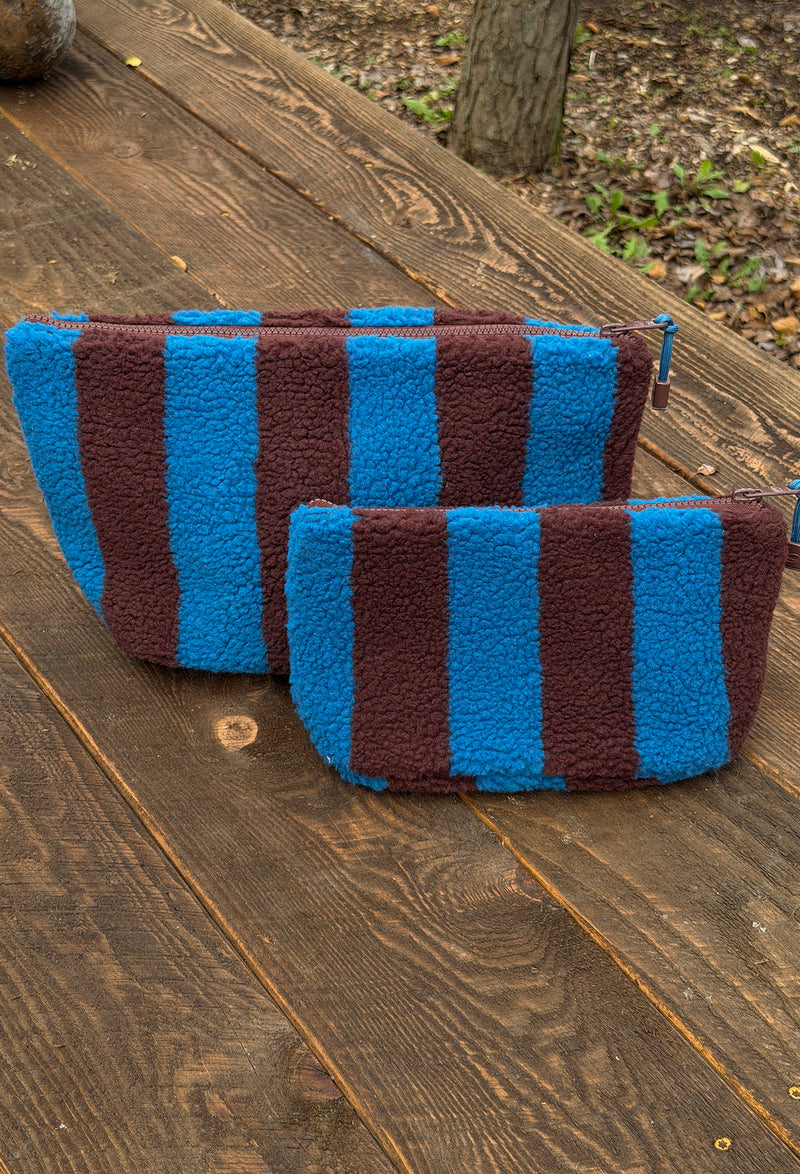 Two striped fleece pouches in bright blue and dark brown, placed on a rustic wooden deck outdoors.
