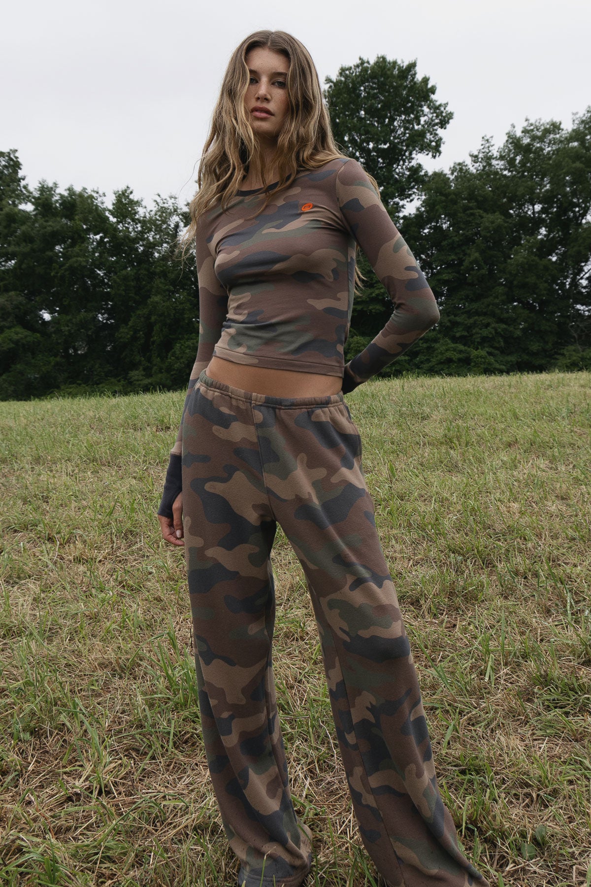 A woman standing in a field wearing matching camo long sleeve top and sweatpants
|M1