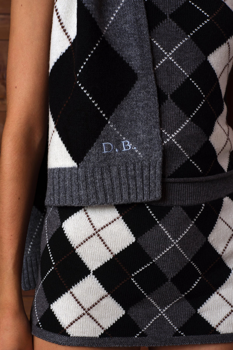 Close-up of a dark gray ribbed knit skinny scarf with a black, white, and gray argyle pattern, featuring the embroidered initials 'D.B.