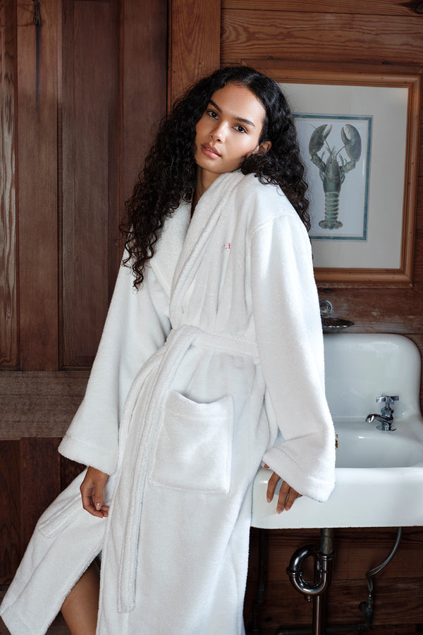 Woman in a white robe standing in a bathroom with wooden walls and a sink.
|M1