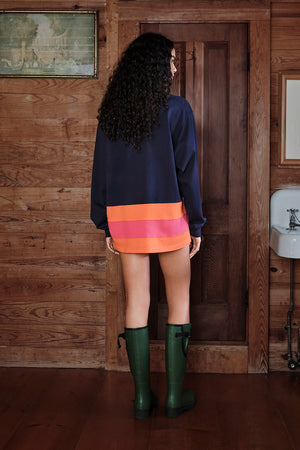 Person wearing a navy sweater, orange skirt, and green boots standing in a wooden interior.
|M1