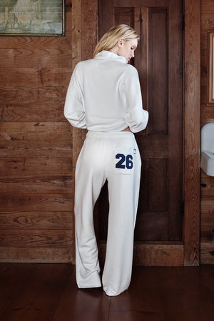 Woman wearing a white sweatsuit with number 26 on the back pocket in a wooden interior setting
|M1