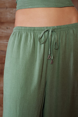 Green linen pants with a drawstring and brand logo on a wooden background
|M1