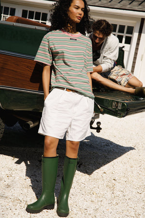 Person wearing a striped shirt, white shorts, and green rain boots standing next to a vintage truck.