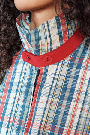 Close-up of a person wearing a plaid shirt with a red collar and buttons.
|M1