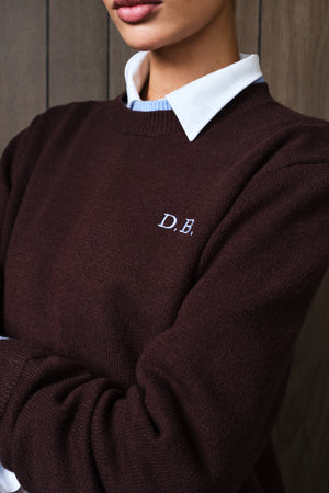 A close-up of a person wearing a dark brown knit sweater with a white embroidered 'D.B.
|M1