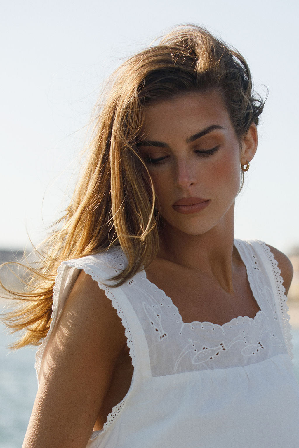 Woman wearing a white sleeveless dress with lace details against a blurred natural background
|M2