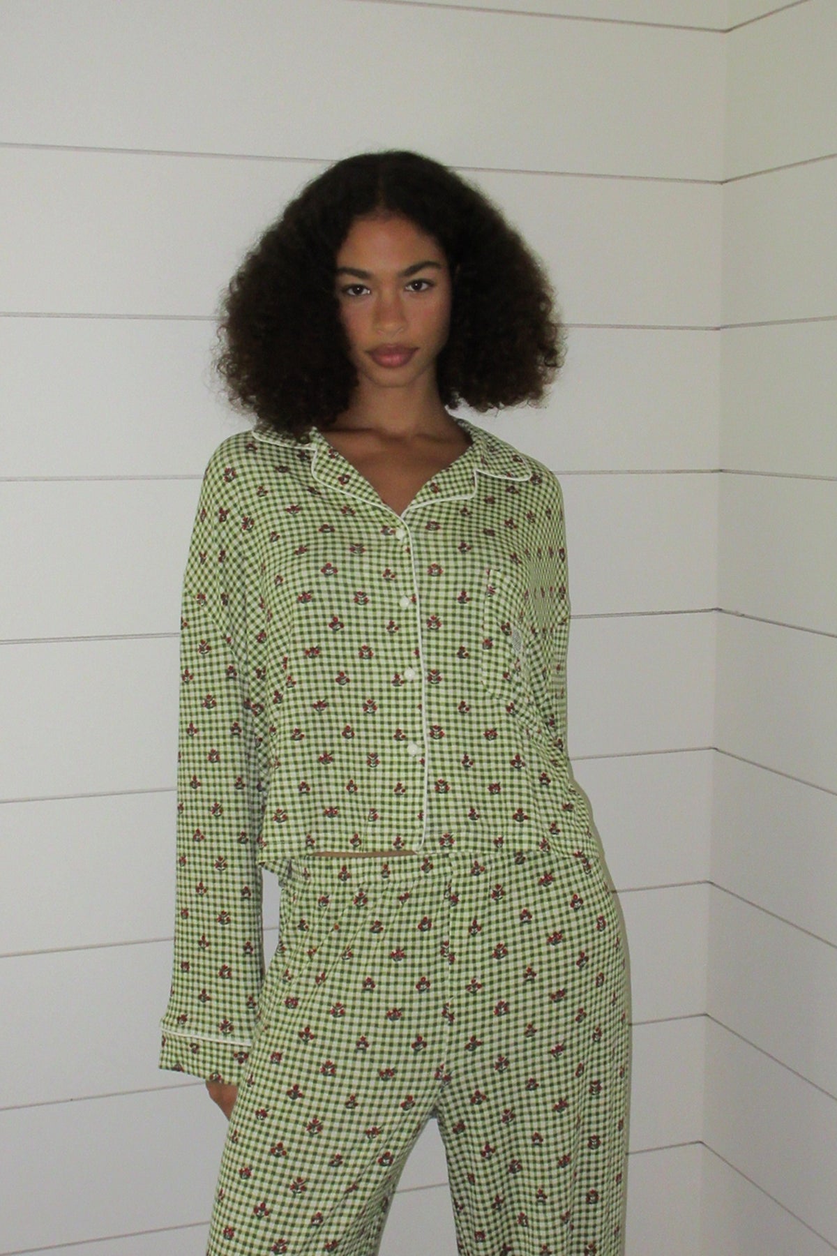Green and white gingham pajama set with a small red floral print, white piping, button front and chest pocket, front view on a model. |M1