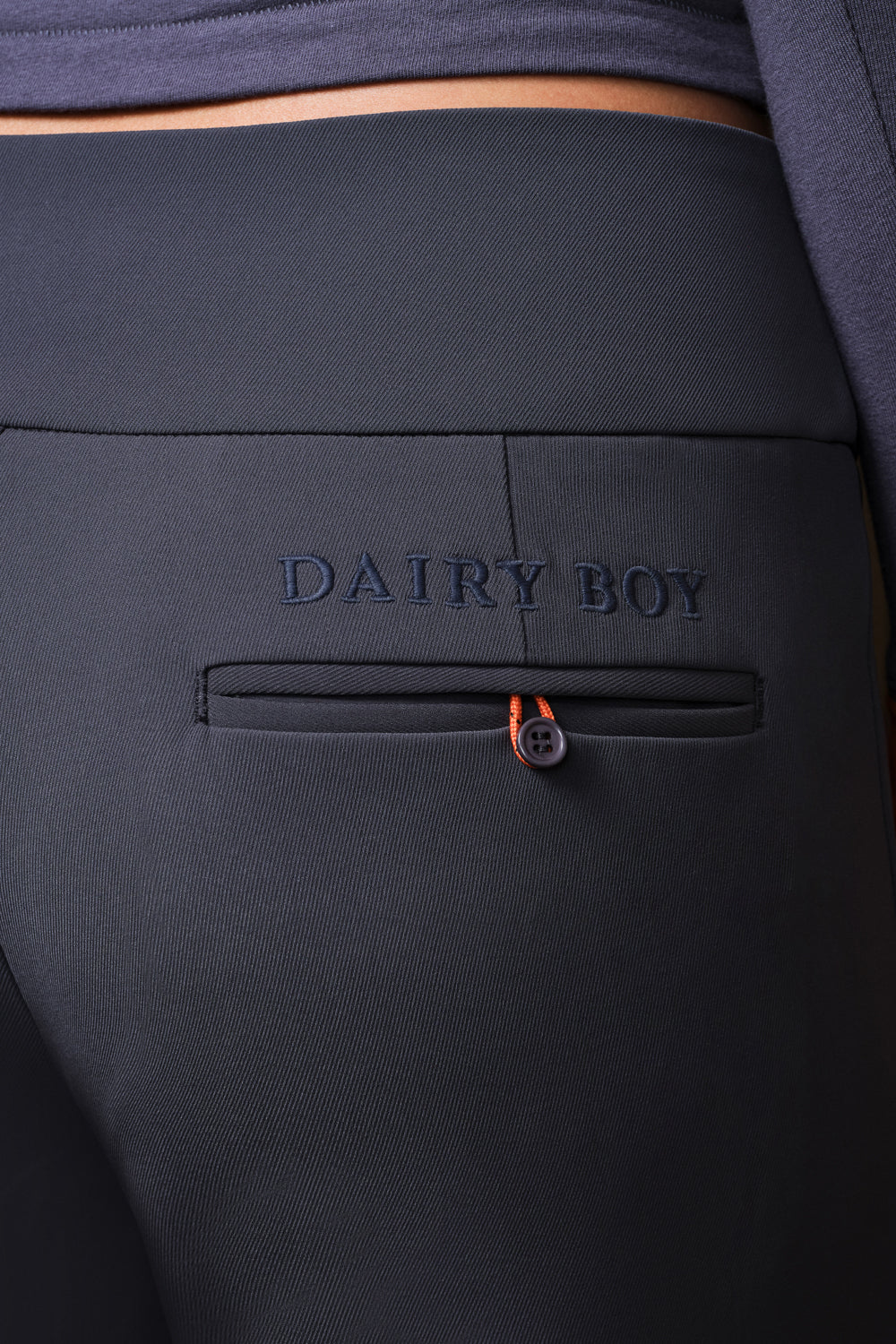 Close-up of dark charcoal gray pants featuring an embossed 'DAIRY BOY' logo on the back pocket, with a small orange accent near the pocket closure.
|M1