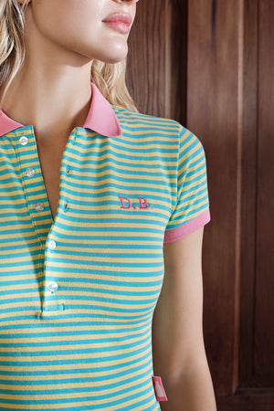 Woman wearing a striped polo shirt with pink collar and trim, featuring a logo on a wooden background.
|M1