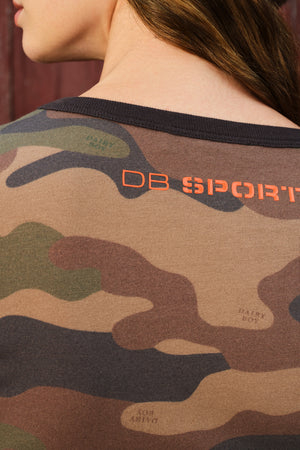 Close-up back view of a person wearing a camouflage t-shirt with a black crew neck and orange 'DB SPORT' text printed on the upper back.