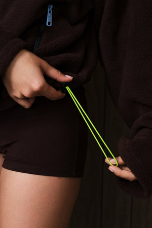 Close-up of a person wearing a dark brown fleece zip jacket and matching shorts, pulling the drawstring of the jacket with one hand.
|M1