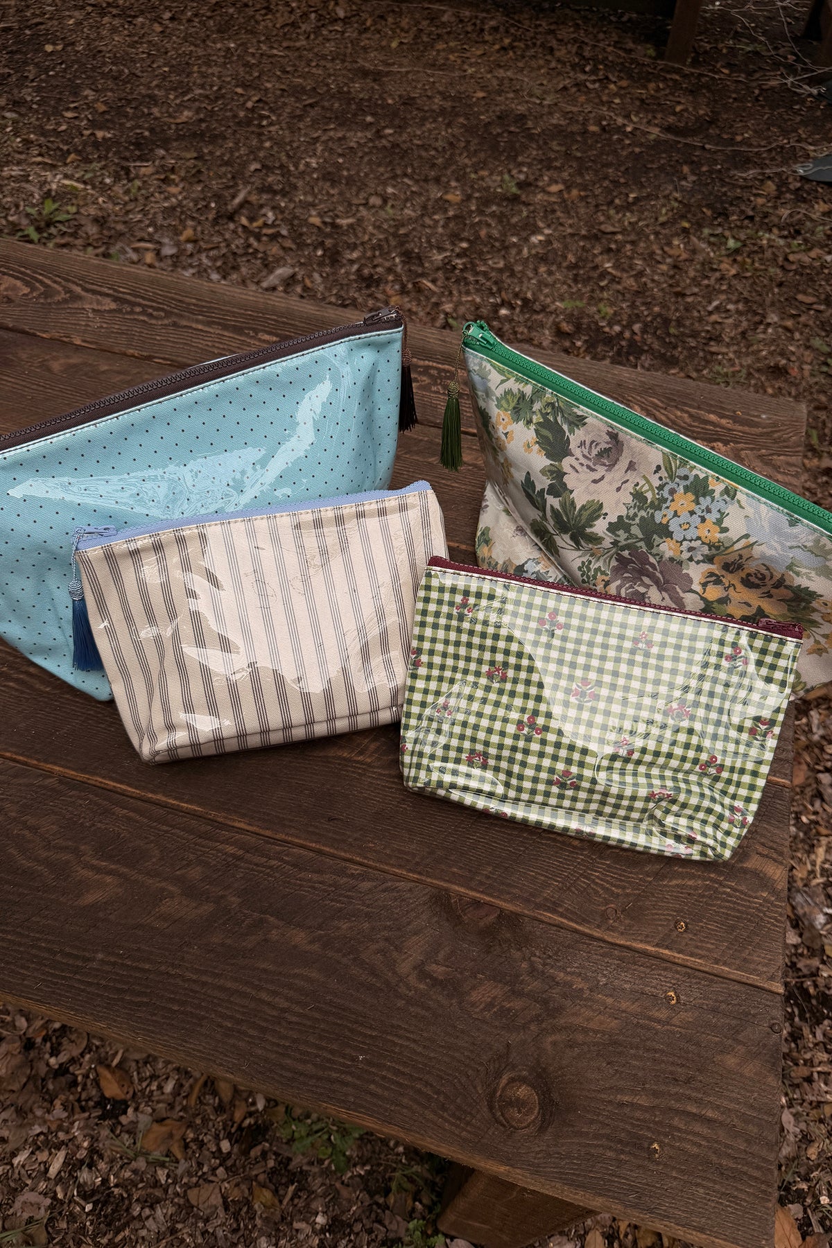 Makeup bag in a muted floral print of roses and leaves with a bright green zipper and green tassel, shown with three other pouches.