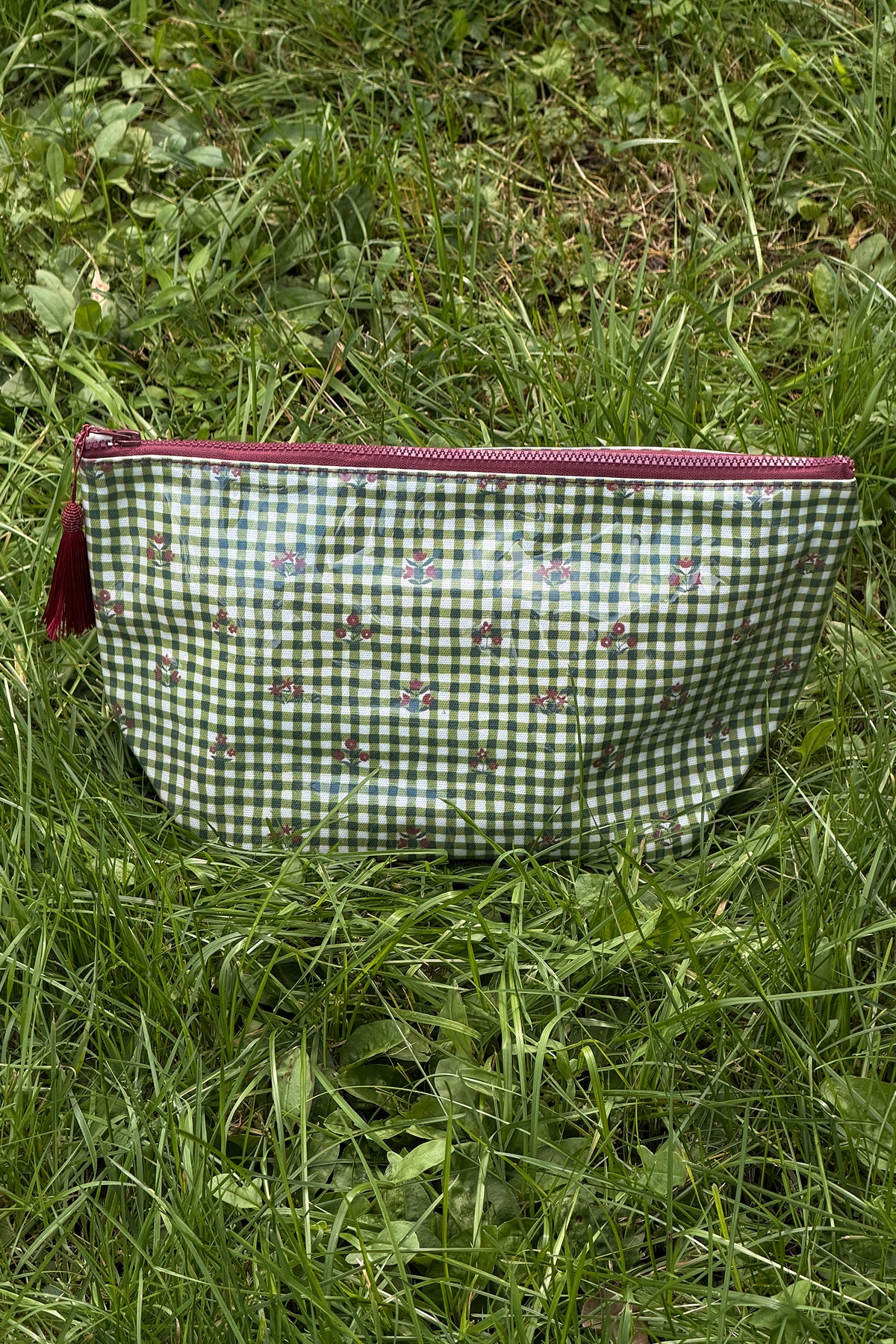 Green and white gingham makeup bag with small red floral motifs, a burgundy zip and a burgundy tassel, shown front on.