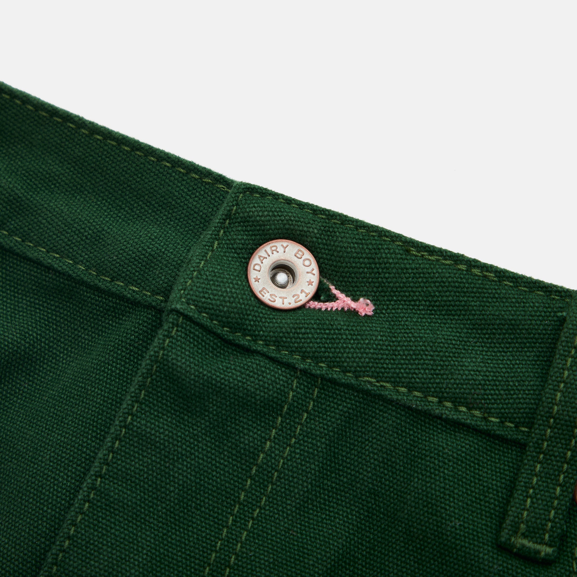 Close-up of a green fabric with a button and brand logo on a white background