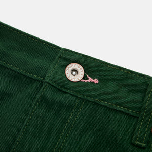 Close-up of a green fabric with a button and brand logo on a white background