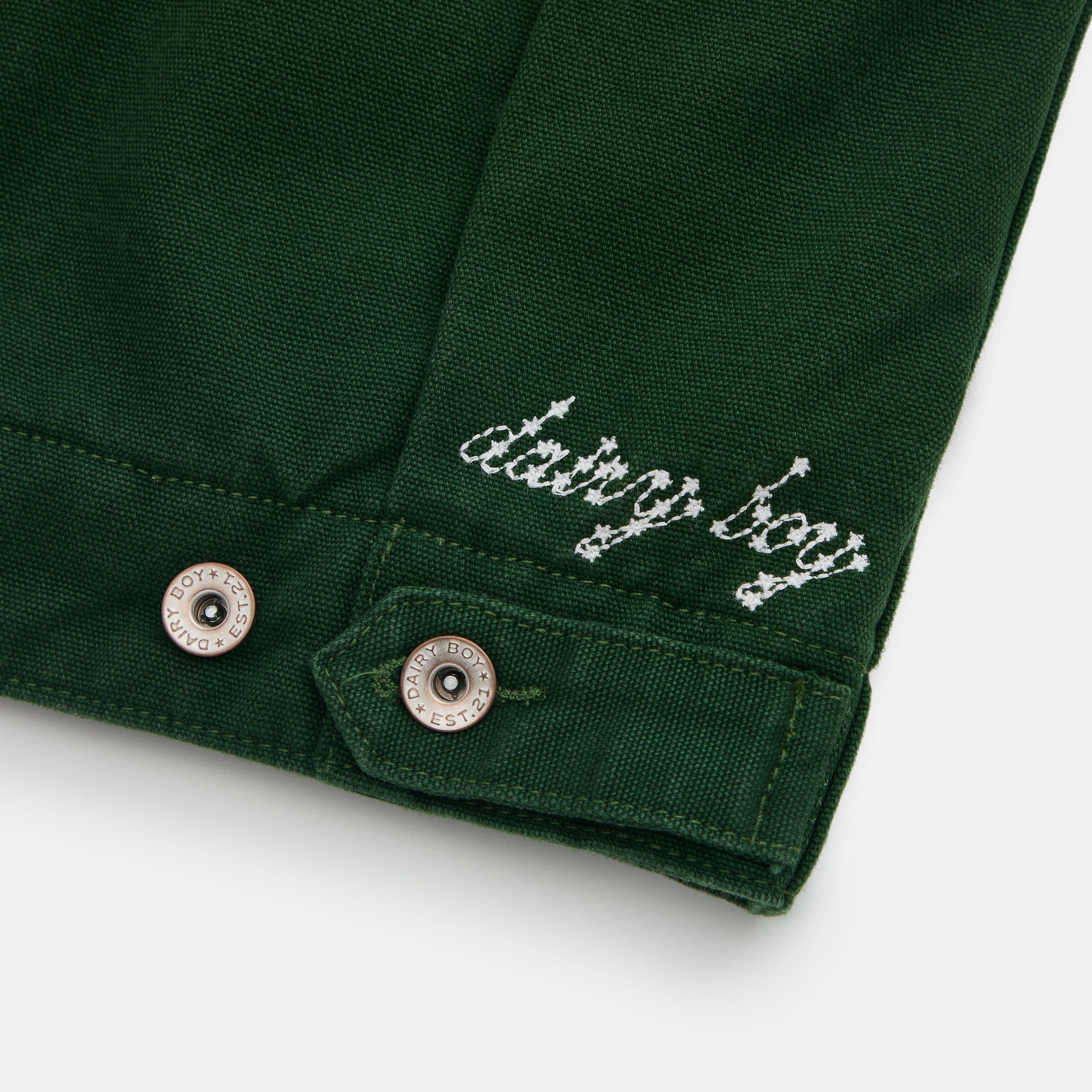 Close-up of a green garment with 'dating boy' embroidery on a white background