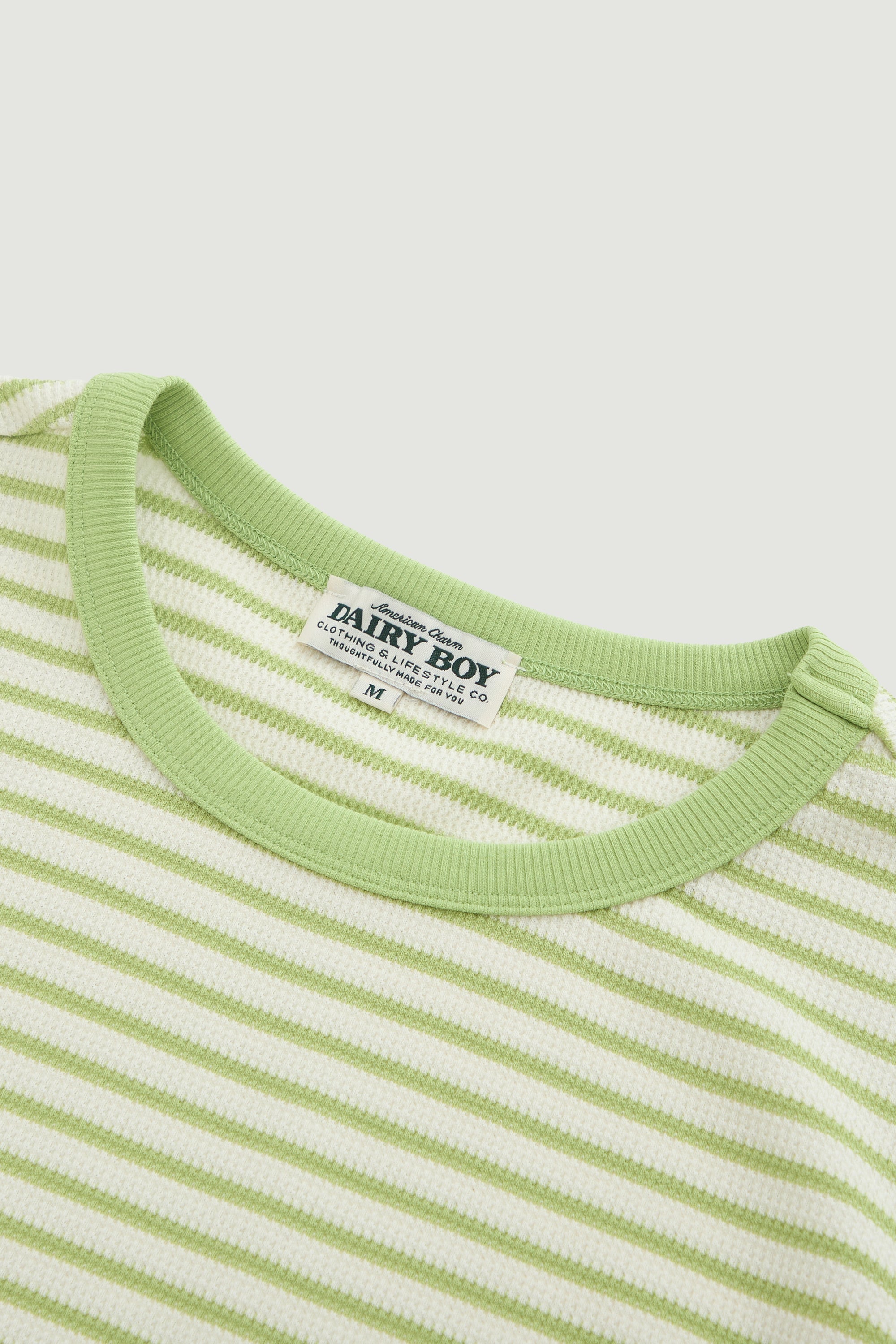 Close-up of a green and white striped shirt with a 'Dairy Boy' label on a light gray background.