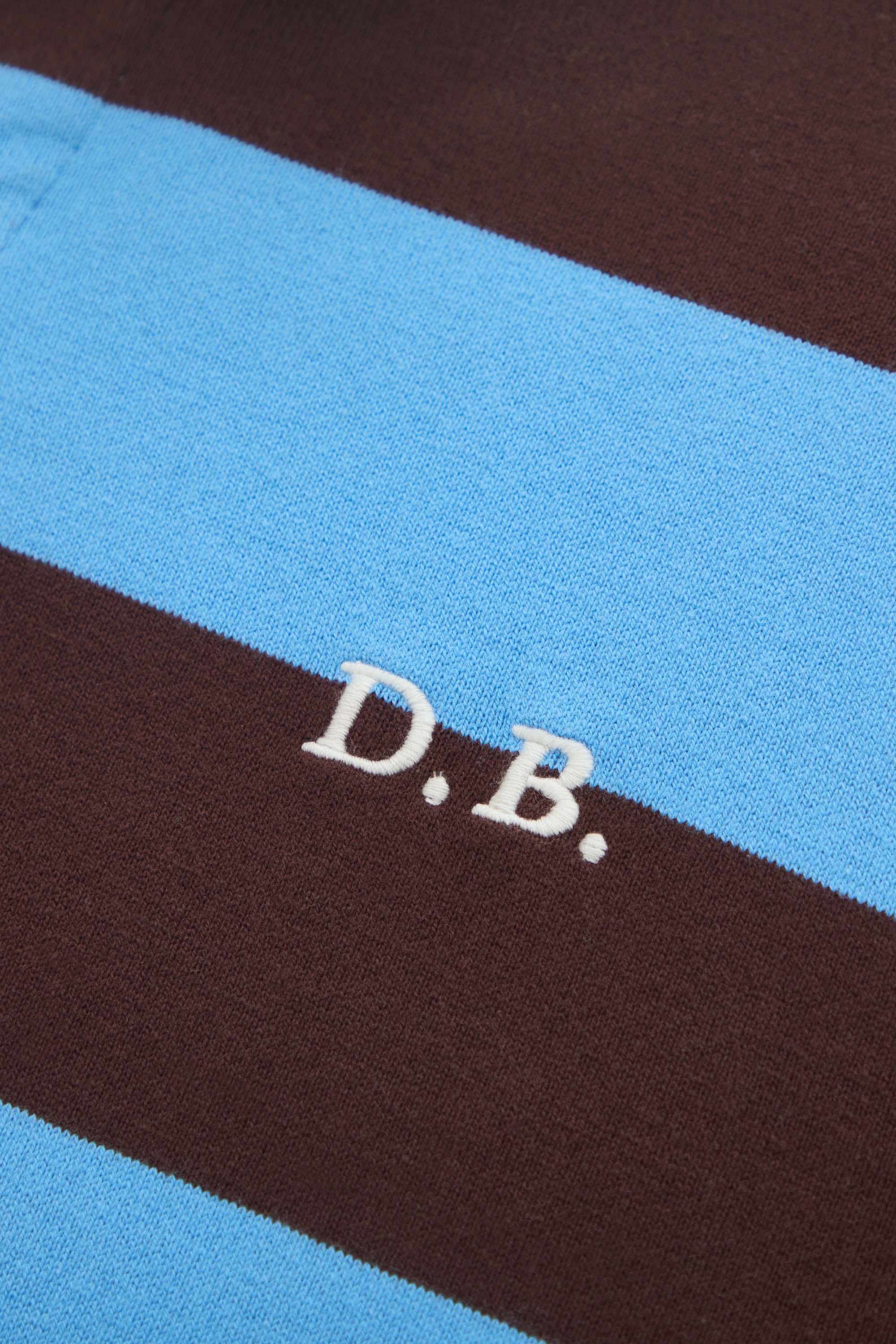 Close-up of a fabric with 'D.B.' embroidery on a blue and brown striped background