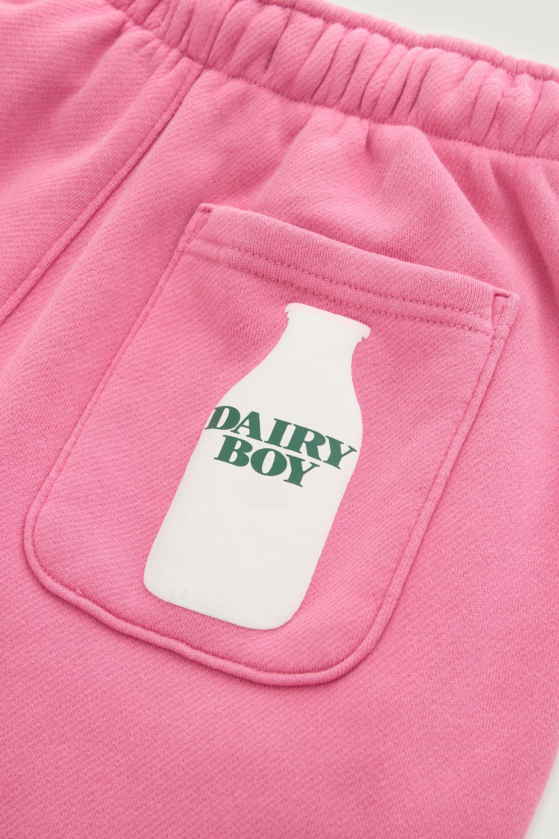Close-up of the Dairy Boy Milk Bottle Sweatpant in Strawberry Milk, showing a soft, stretchy pocket with a white milk bottle graphic and "DAIRY BOY" in green text, plus visible stitching.