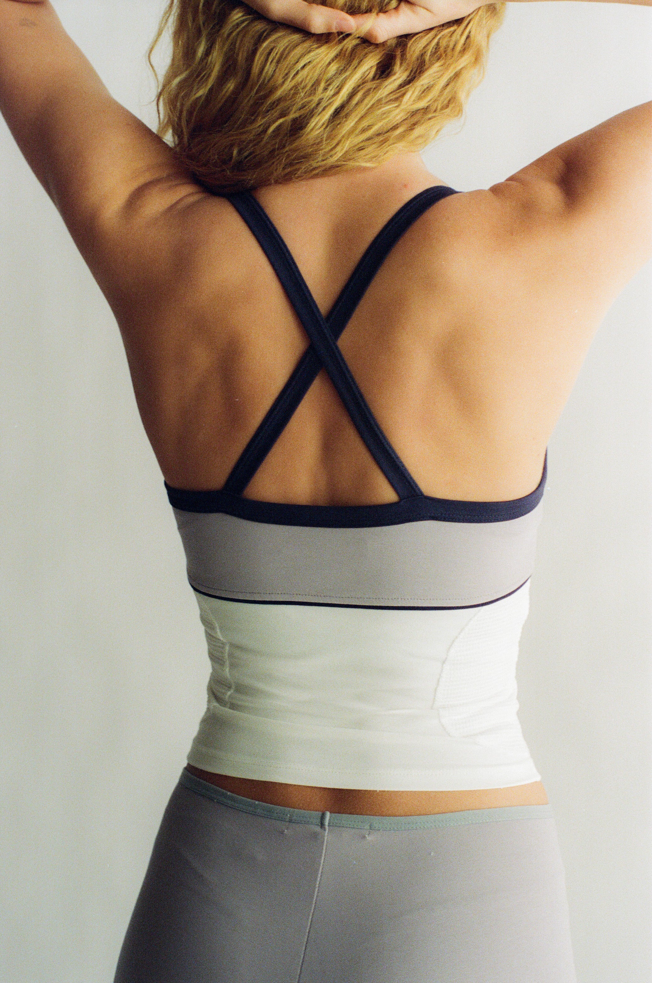 Person wearing a sports top with criss-cross back design on a plain background |M1