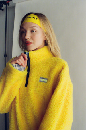 Person wearing a yellow fleece pullover with a visible brand logo, standing against a plain background.  |M1