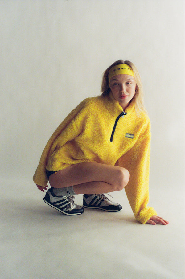 Person wearing a bright yellow fleece pullover with a visible brand logo on a plain background  |M1