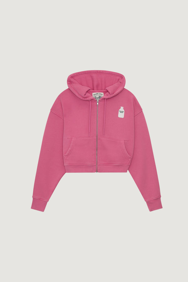 The Dairy Boy Milk Bottle Cropped Zip Up in Strawberry Milk is a bright pink, cropped zip-up hoodie with a front pocket and a small white milk carton graphic on the left chest, shown against a plain white background.