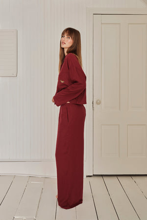 Woman wearing a burgundy pajama set standing in a room with white walls and a door. |M1