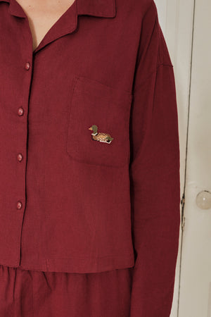 Maroon pajama shirt with a small pocket and decorative button on a plain background. |M1