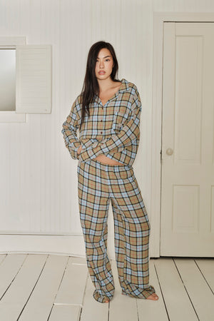 Woman wearing a plaid pajama set standing in a room with white walls and wooden floor. |M1