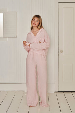 Woman wearing a pink gingham sleep set in a minimalistic room with white walls and wooden floor. |M1