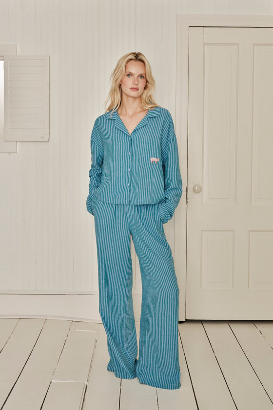 Woman wearing a blue striped pajama set standing in a room with white walls and wooden floor. |M1