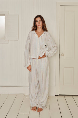 Woman wearing a striped shirt and pants in a minimalistic room with white walls and wooden floor. |M1