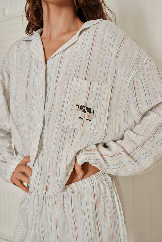 Person wearing a striped shirt with a pocket featuring a cow design against a white background. |M1