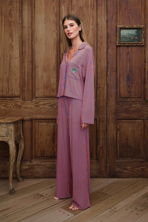 A woman stands barefoot in a rustic room with wooden paneling, wearing a matching pajama set with orange and blue vertical stripes. The set includes a long-sleeve button-up top and wide-leg pants.
|M1