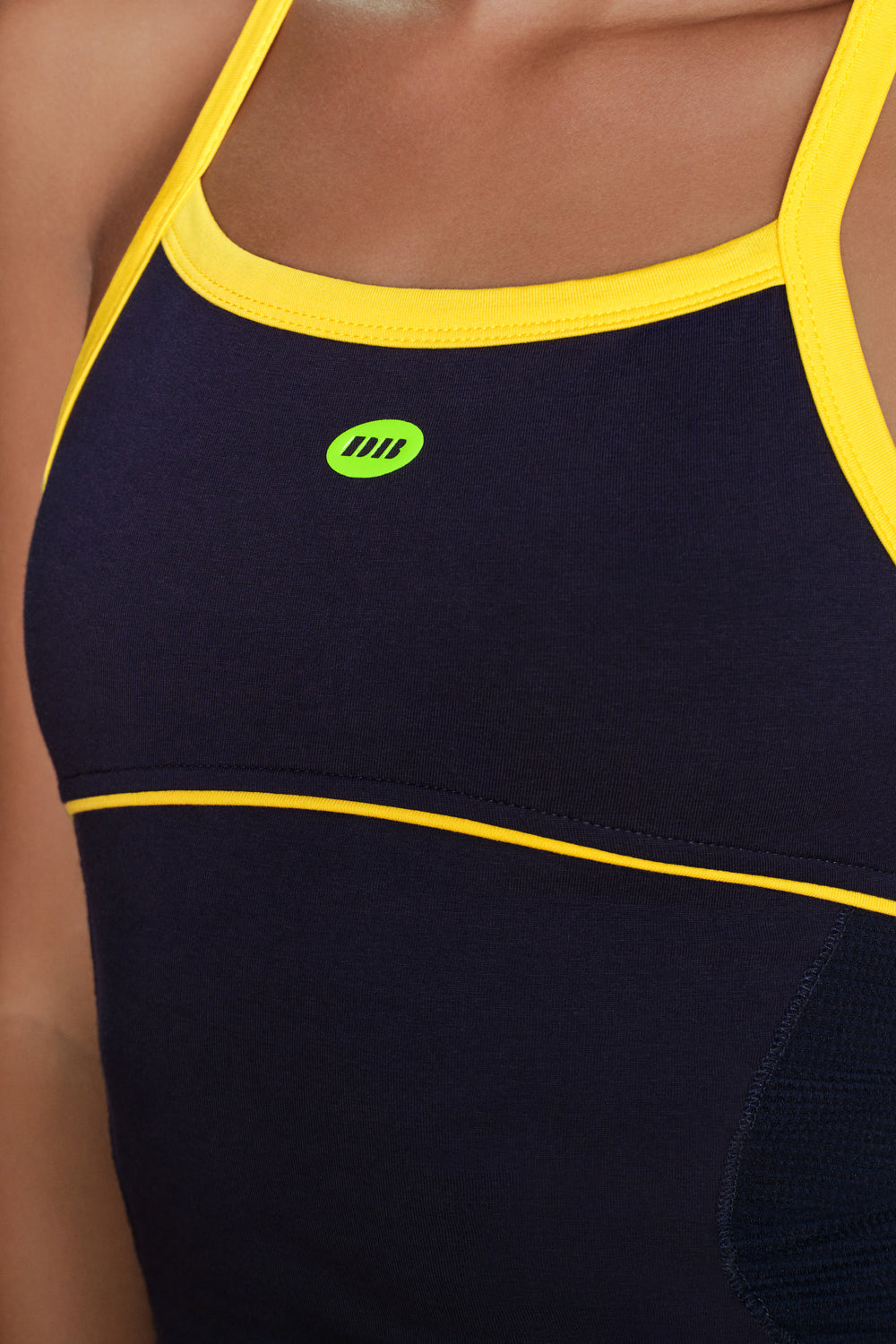Close-up of a dark navy athletic tank top with bright yellow trim and a small green logo on the chest, worn by a model.
|M1