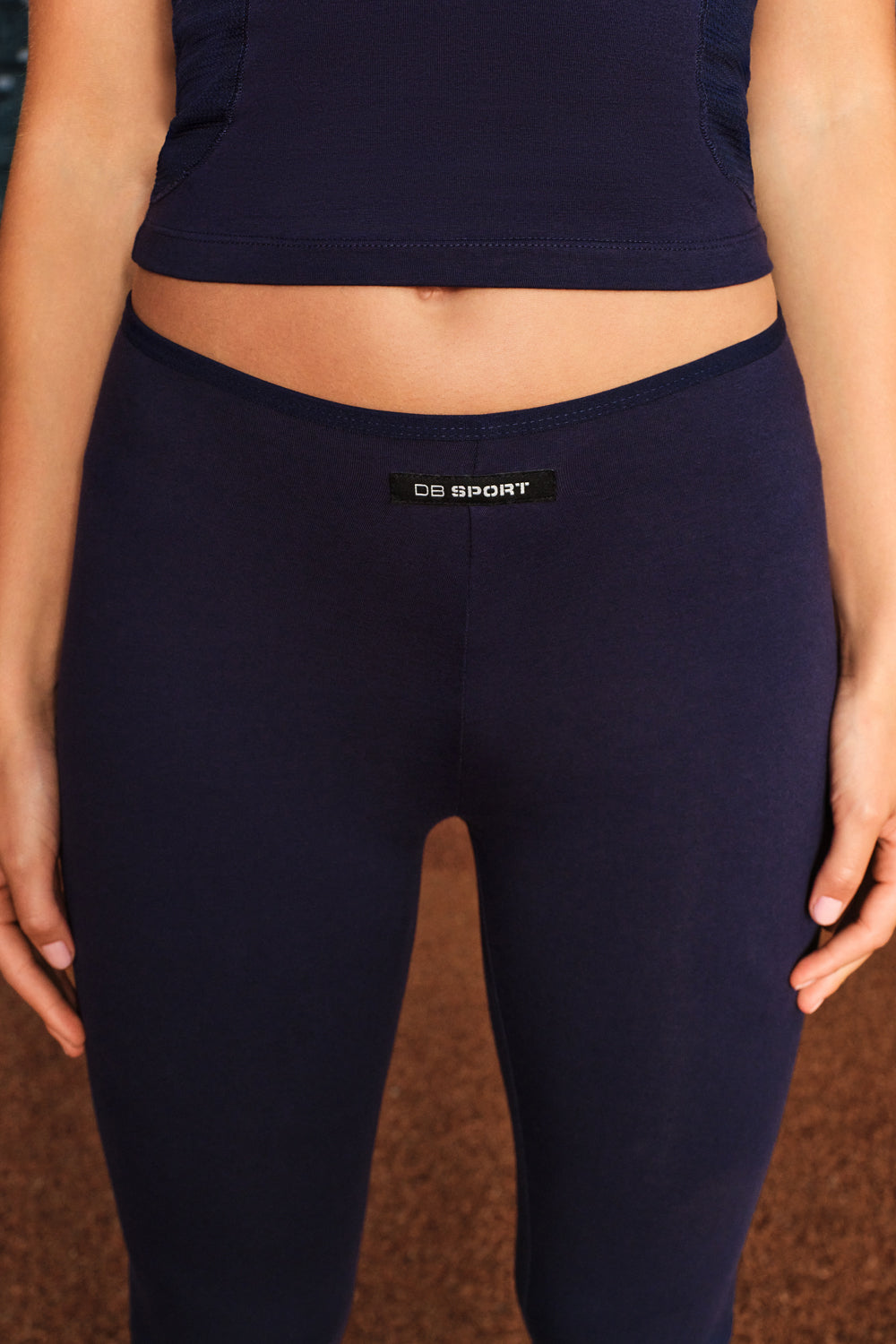 Close-up of a person wearing dark navy leggings with a small black waistband label reading 'DB SPORT'.
|M1