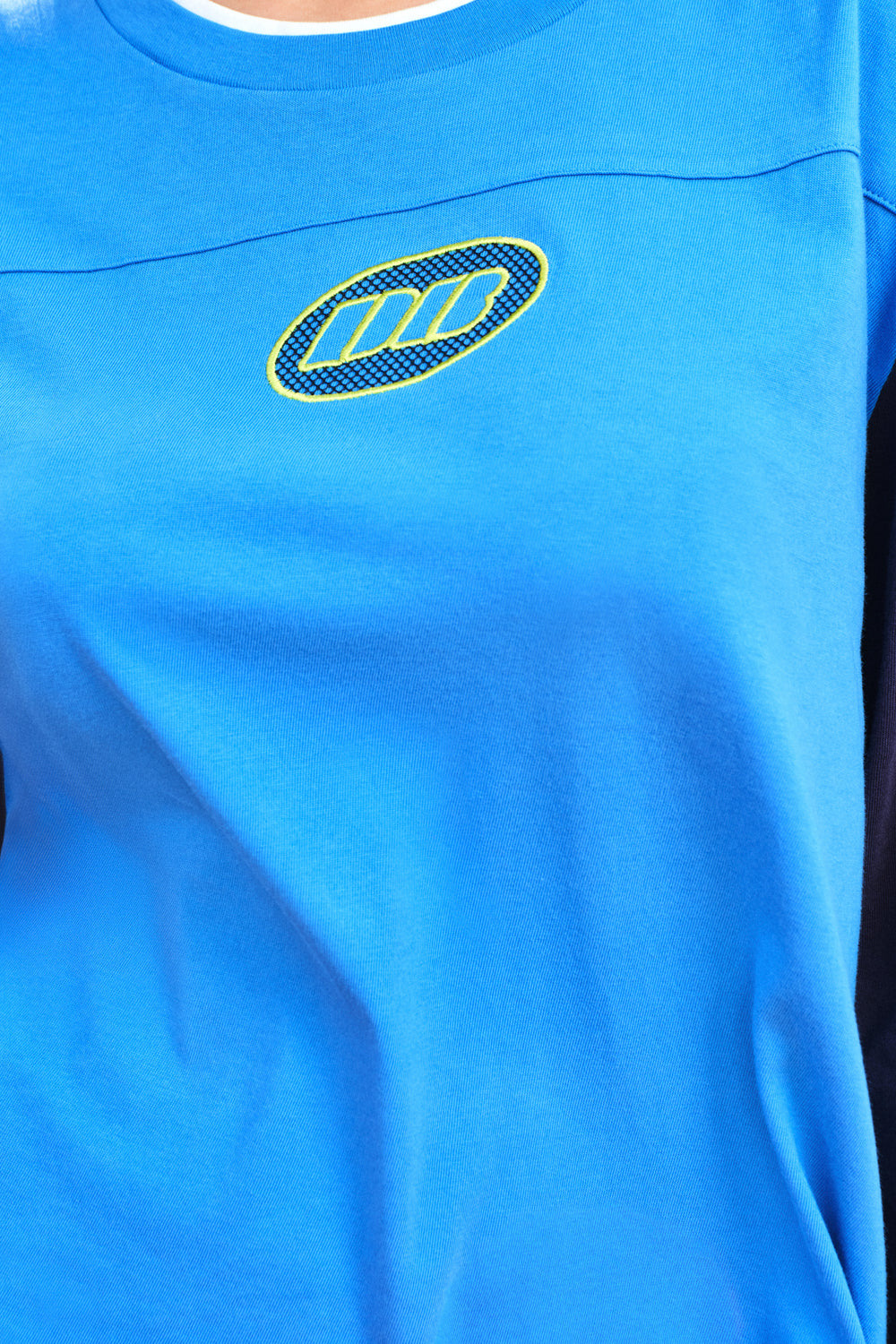 Close-up of a bright blue athletic top with a yellow and black embroidered logo on the chest.
|M1
