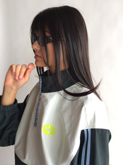 Person wearing a white jacket with a logo, standing against a plain background |M2
