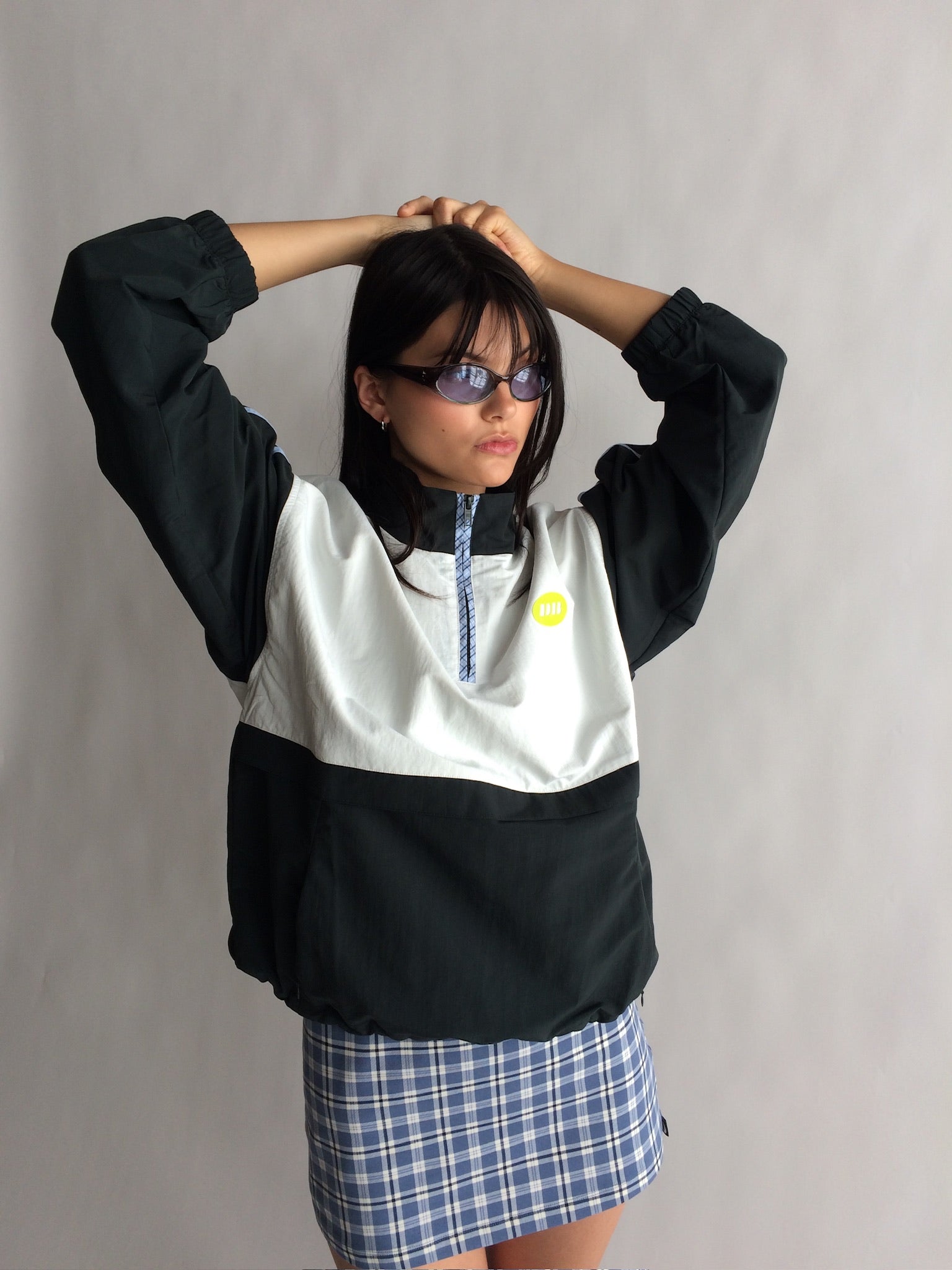 Person wearing a black and white jacket with a plaid skirt against a plain background |M2